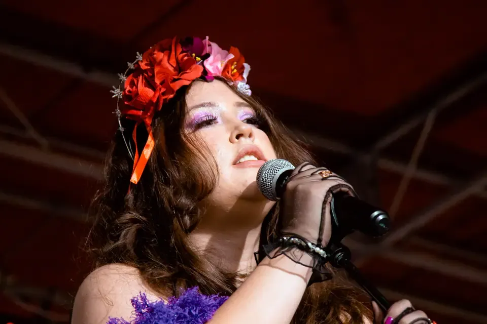 Ginger Rodriguez singing into a microphone at the Viva La Vida Festival in Austin on October 30, 2022, wearing a floral headdress and a purple wrap.