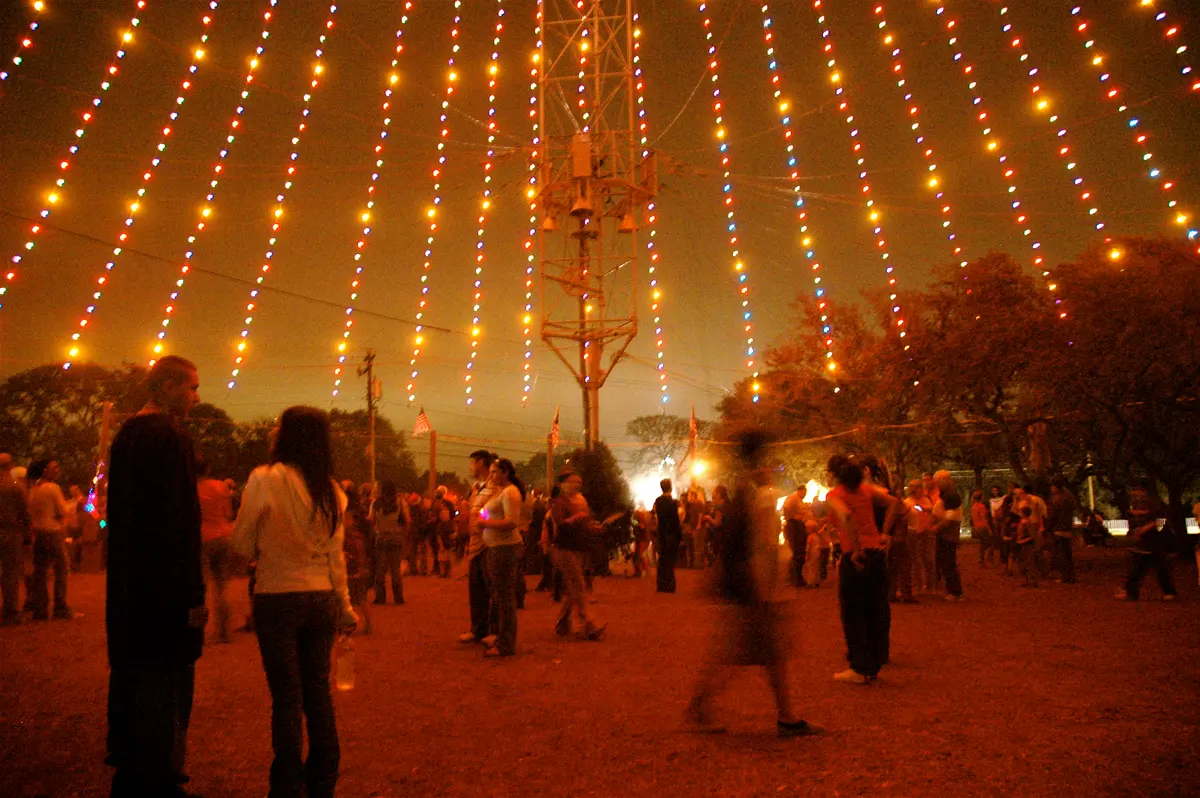 People walking at night under the Zilker Holiday Tree during the Trail of Lights in Austin on December 18, 2006, with colored light strings hanging from a metal tower.